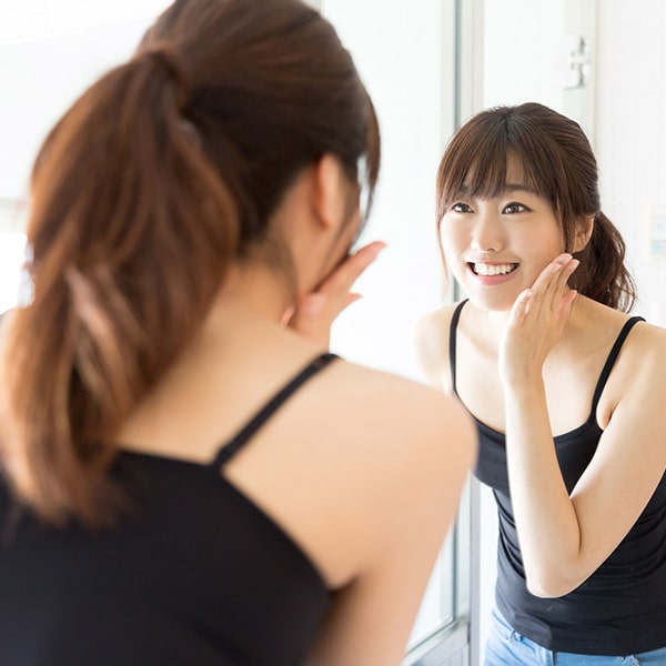 A young woman looking in the mirror while touching her face and smiling
